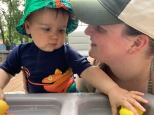 A young mother looks on and smiles at her baby boy